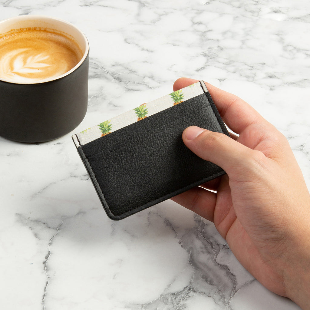 Black Rahui Juniper card wallet made from Pinatex plant leather being held by hand on marble side with coffee cup