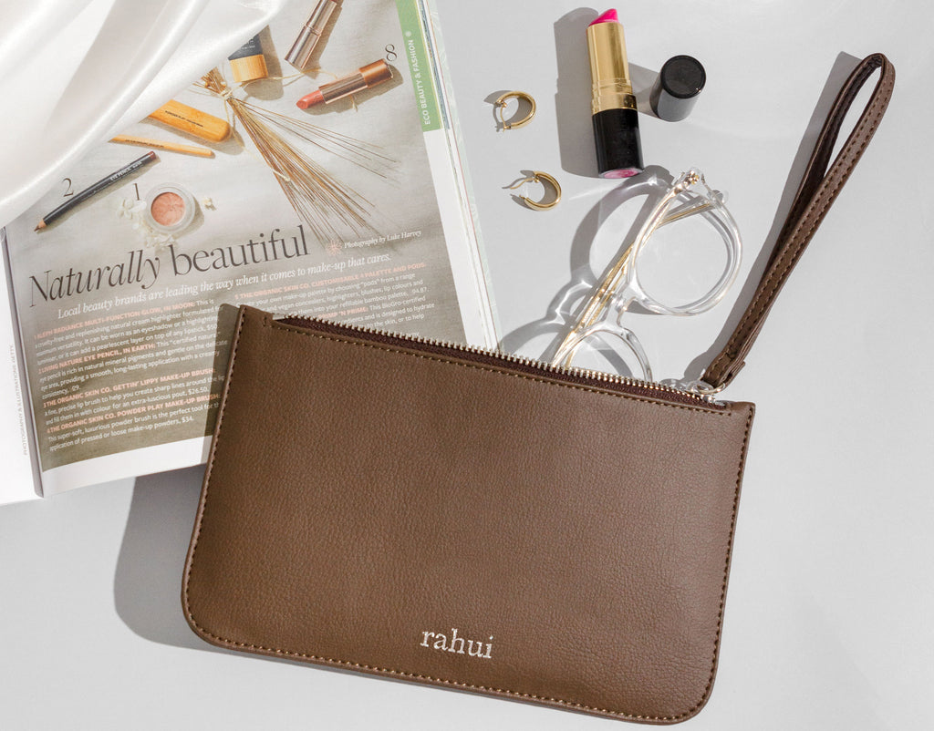 Brown Rahui Clutch on white background next to magazine, glasses and lipstick