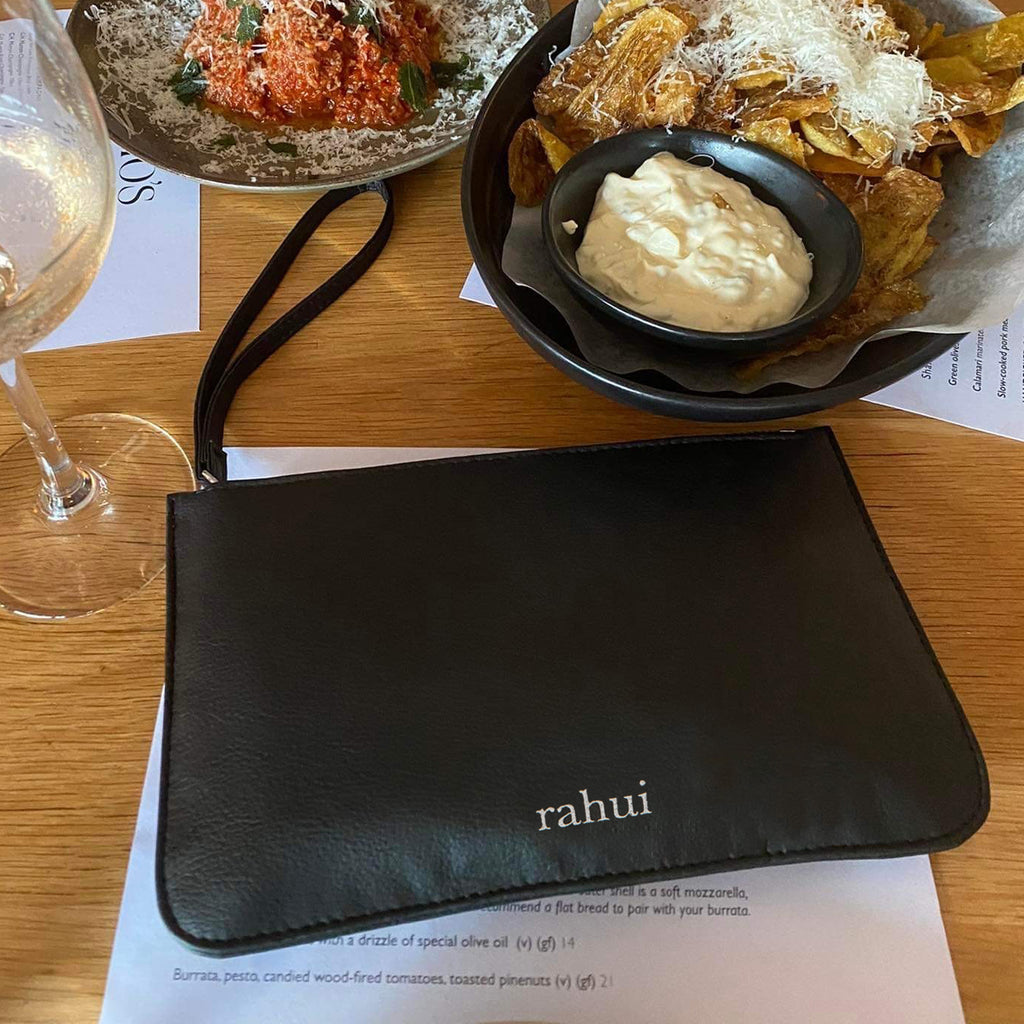 Black Rahui Clutch on table next to wine glass and plate of vegan foods
