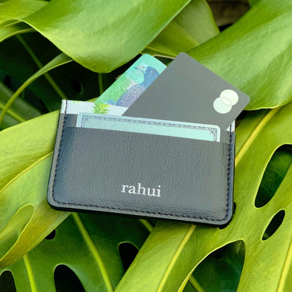 Black Rahui Juniper card wallet with credit card and cash sitting on a green leaf