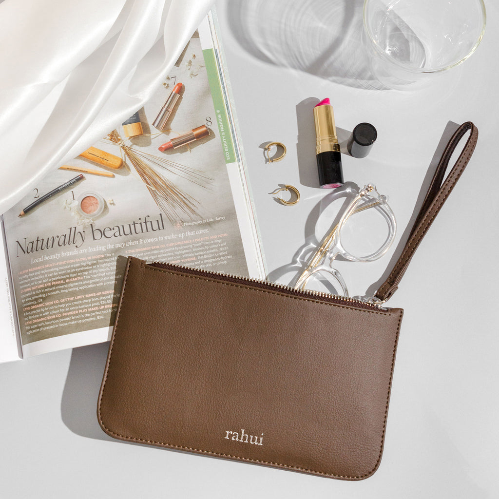 Brown Rahui Clutch on white background next to magazine, glasses and lipstick