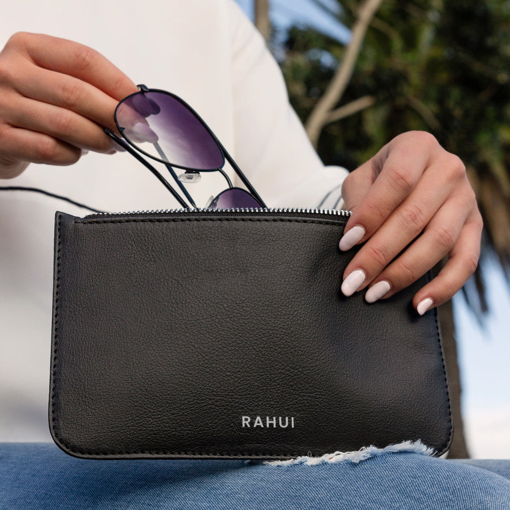 Close up of female hands taking sun glasses out of a black Rahui clutch