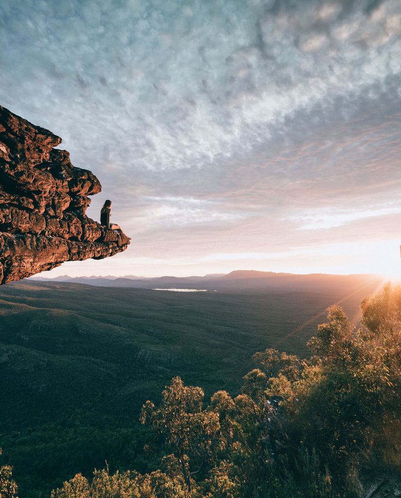 Person sitting on rock overlooking trees, watching the sunset