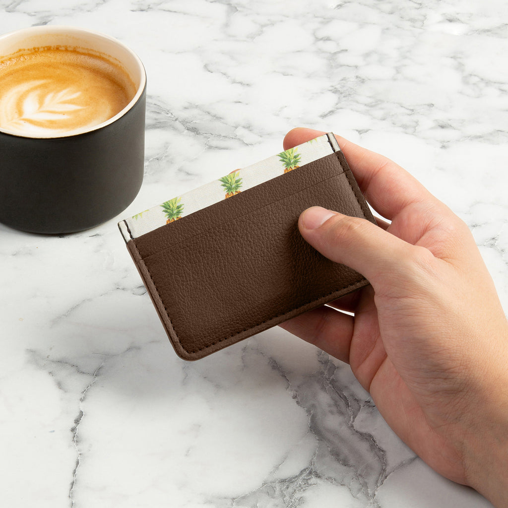 Brown Rahui Juniper card wallet made from Pinatex plant leather being held by hand on marble side with coffee cup
